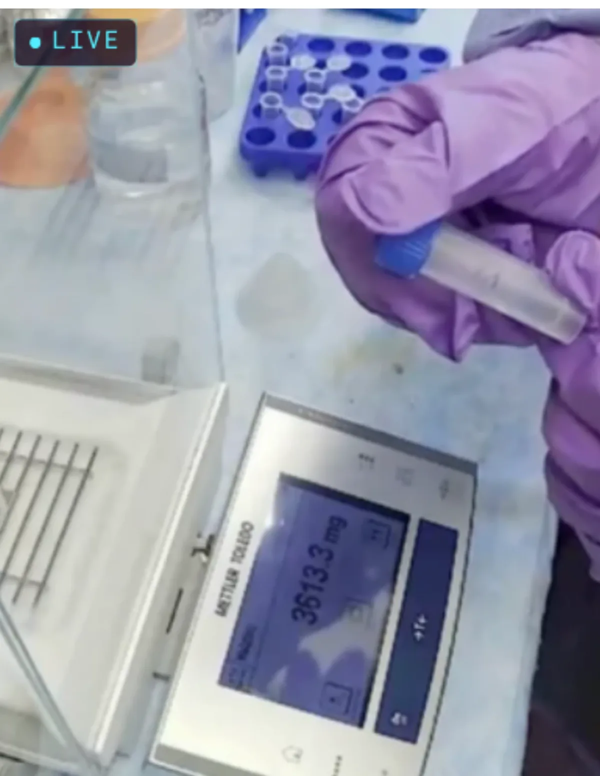 A scientist weighing a sample tube on an analytical balance while VERA records live